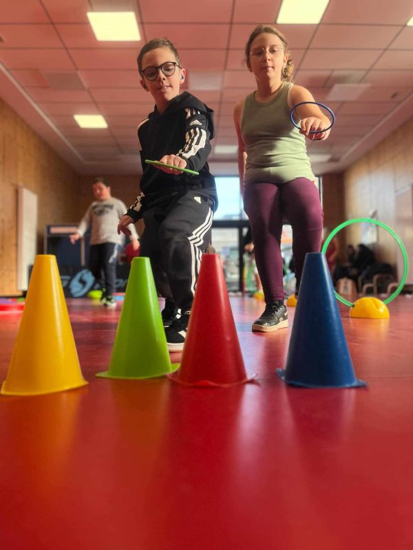 deux enfants vont déposer sur des cônes des anneaux le plus vite possible sur leur parcours sportif.